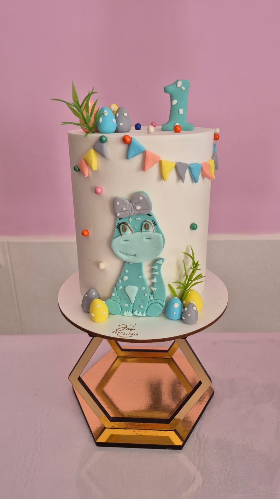 Torta infantil decorada con un dinosaurio, banderines y colores pastel, hecha por Jor.